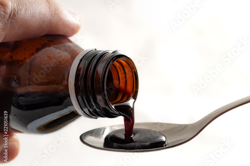 Cold and flu treatment and bitter medicine concept with close up on hands pouring cough syrup from a brown glass bottle in a teaspoon isolated on white background