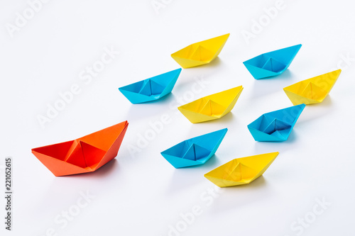 Leadership, influencer, KOL, key opinion leader new marketing channel concept, big red paper ship origami lead in front of others small yellow and blue fleet on white background photo