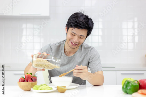 Attractive handsome young guy pour cereal from glass bottle to bowl for making breakfast in morning. Handsome man hold wooden spoon. Charming handsome guy gets happy and enjoy meal. It good for health