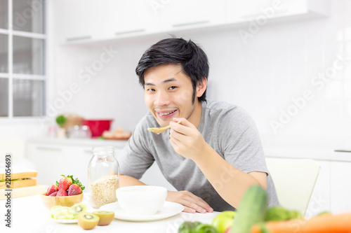 Attractive handsome man eat breakfast or cereal  fruits  milk on table in kitchen at house in morning. Handsome guy gets happy with smile. Lovely asian man take care his self well by eating good meal