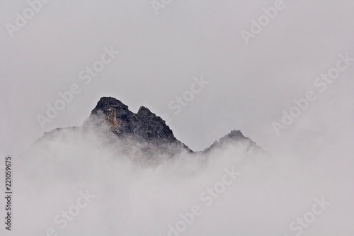 Fotografie a mountain peak peeks through fog and mist seeming to float in the sky in southe
