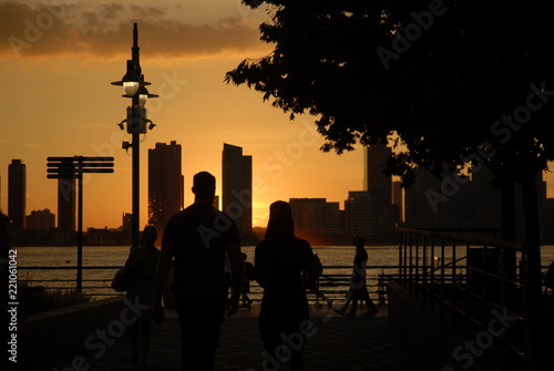 Sunset over a cityscape on the water; people walking