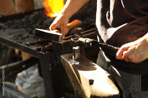 The blacksmith works with anchor metal on an anvil with a hammer and ticks