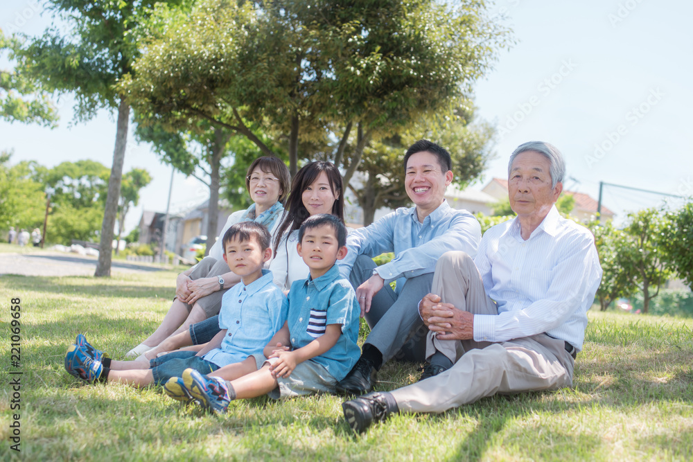 公園で芝に座り微笑む三世代家族