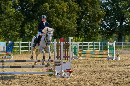 A young woman jockey on a horse performs a jump across the barrier. Competitions in equestrian sport.