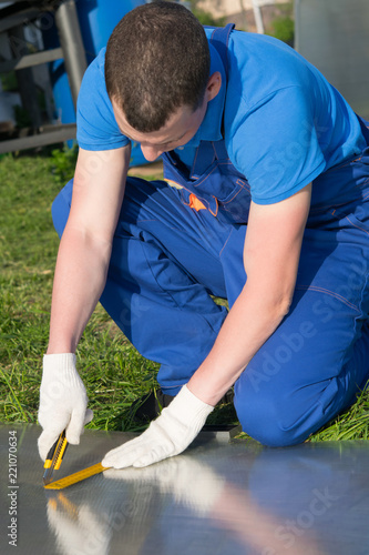 worker in blue uniform, cuts a sheet of decking for the roof