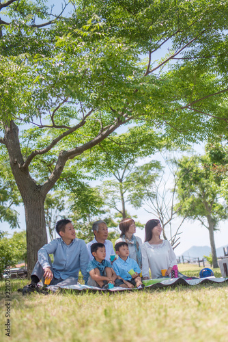 公園でレジャーシートに座りピクニックをする三世代家族