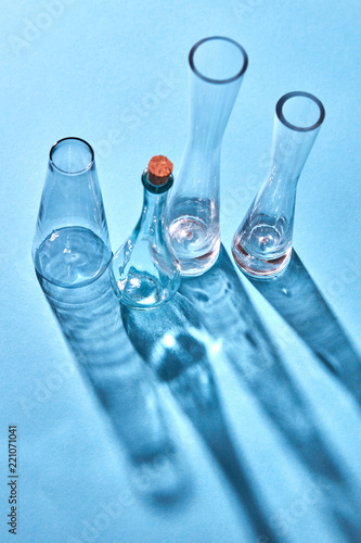 A glass empty bottles on a blue paper background with long shadows and reflection. photo