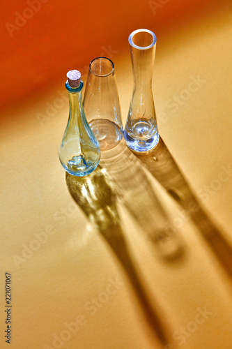 Three glass bottles empty on a duotone yellow paper background with diagonal shadows and reflection. photo