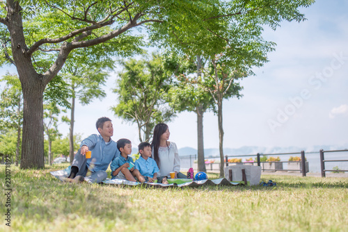 公園でレジャーシートに座りピクニックをする家族 © tomoco_sozai