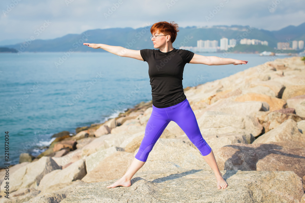 adult woman with short red hair in sportswear doing yoga exercise outdoors with sea views adult woman with short red hair in sportswear doing yoga exercise outdoors with sea views