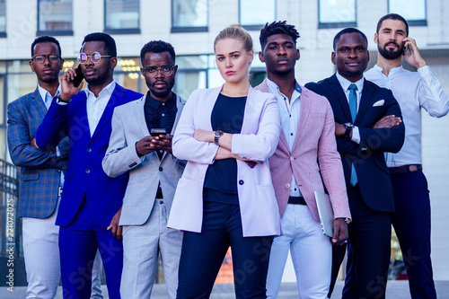 a group of seven successful business people businesslady and her male partners in stylish suits standing and looking proudly outdoors . teamwork and the multiethnic company concept