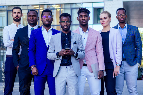 a group of seven successful business people men and woman in stylish suits standing and looking proudly outdoors . teamwork and the multiethnic company concept