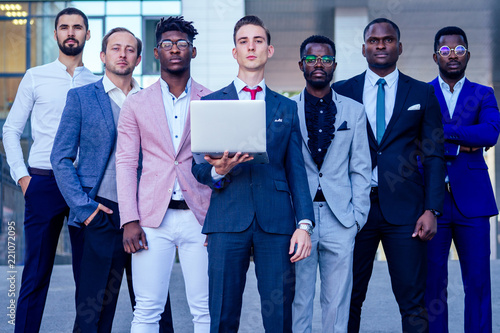 a group of seven successful business people men in stylish suits standing and looking proudly outdoors . teamwork and the multiethnic company concept