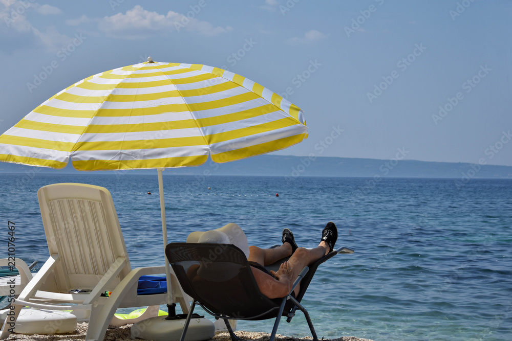 Elder woman sitting at the beach in sun chair under umbrella/ Enjoying the summer/ Summer vacation fun