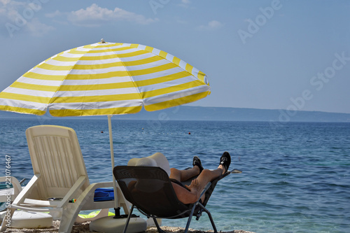 Elder woman sitting at the beach in sun chair under umbrella/ Enjoying the summer/ Summer vacation fun © Sanja