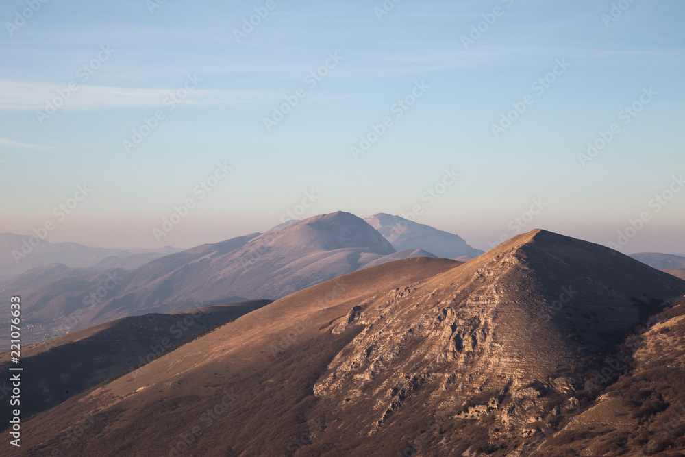 A view of some mountains top, beneath an empty blue sky at golden hour A view of some mountains top, beneath an empty blue sky at golden hour