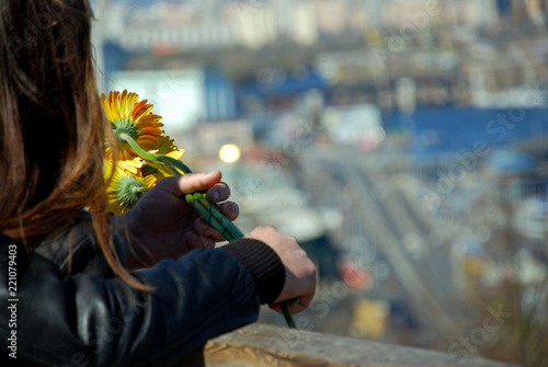 A pair of lovers look at the city from a height. Romantic photography. A bouquet of yellow flowers gerbera in the hands of a girl with long hair. Love. Copy space.