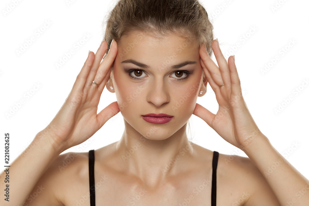 Naklejka premium Portrait of beautiful young woman tightening her face with her hands on white background