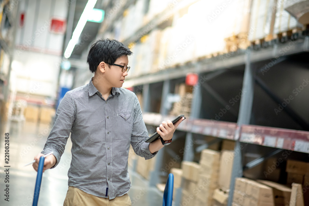 Young Asian man worker doing stocktaking of product in cardboard box on shelves in warehouse by using digital tablet and pen. Physical inventory count concept Young Asian man worker doing stocktaking of product in cardboard box on shelves in warehouse by using digital tablet and pen. Physical inventory count concept