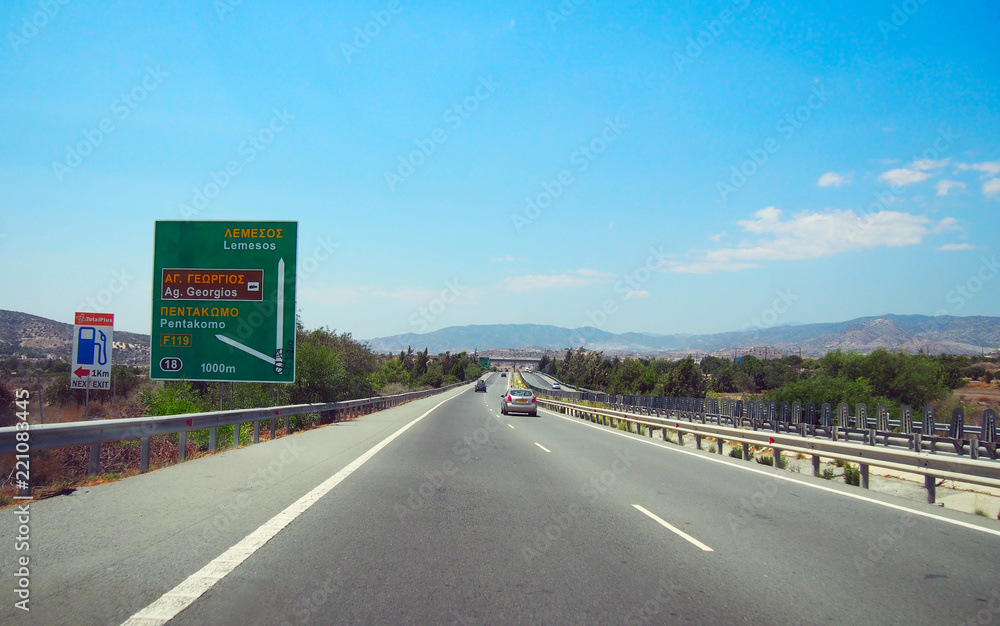 Fototapeta premium Straight motorway in Cyprus with road sign. Bright sunny summer day