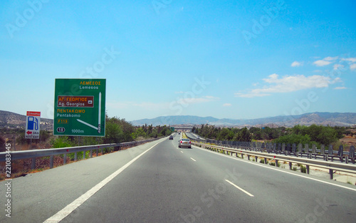 Straight motorway in Cyprus with road sign. Bright sunny summer day