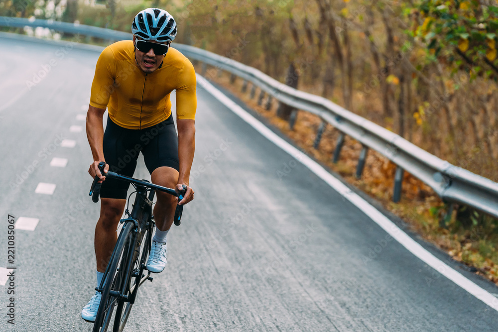 Focus on Asian man wearing a yellow cycling jersey, who's riding a road bike  up high on hill in the morning. Under morning sunshine with determination  on his face. foto de Stock