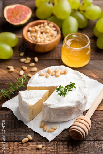 Brie or camembert with pine nuts, figs, honey and green grapes on brown wooden serving board. Closeup view, selective focus