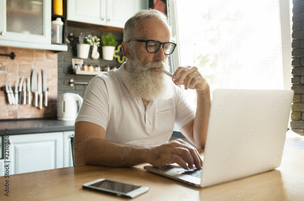 Senior man holding a Electronic Cigarette while using a laptop. IQOS. Senior man holding a Electronic Cigarette while using a laptop. IQOS.