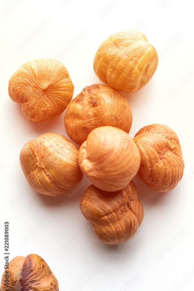 Pile of hazelnuts placed in a the middle on white background lighted with sun. Creative concept of health and wellness. Nuts. Selective focus Pile of hazelnuts placed in a the middle on white background lighted with sun. Creative concept of health and wellness. Nuts. Selective focus