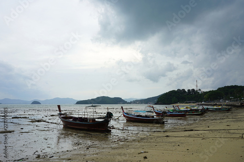 Fisherman boat parking on the lower tide beach with the dull sky background