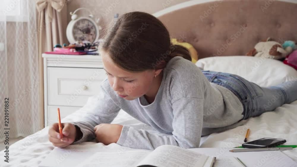 Cute little girl lying on bed and doing homework Cute little girl lying on bed and doing homework