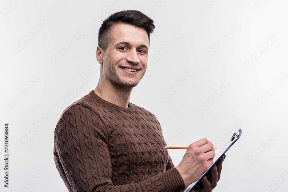 Male secretary. Smiling dark-haired male secretary wearing brown sweater making notes on image without face retouching