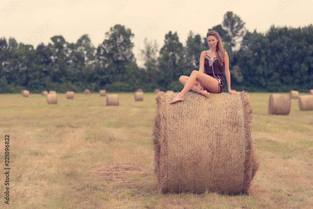 Beautiful woman sitting on hay bale a summer's day Beautiful woman sitting on hay bale a summer's day