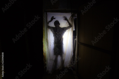 Human silhouette behind packing film in dark creepy room of abandoned building