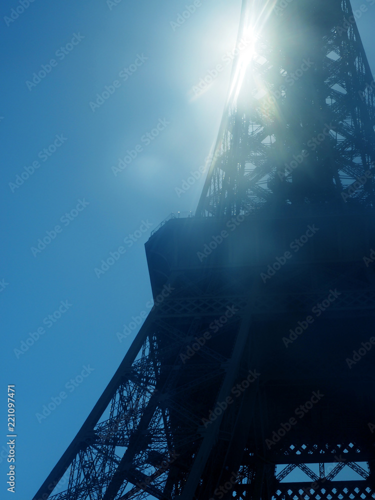 Paris, France. Sun shining through Eiffel Tower. Sun beams and spots. Blue sky, fragment of a design of the Eiffel Tower, one of the most visited and recognizable sights of the world