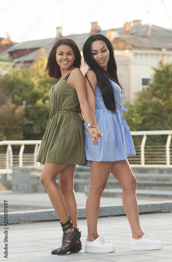 Outdoors portrait of two female multiethnic friends. Girls in casual outfits having a walk in the city, having fun and hugging, copy space. Urban lifestyle, friendship concept Outdoors portrait of two female multiethnic friends. Girls in casual outfits having a walk in the city, having fun and hugging, copy space. Urban lifestyle, friendship concept