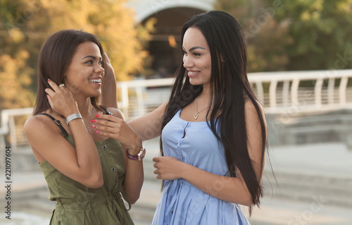 Outdoors portrait of two female multiethnic friends. Girls in casual outfits having a walk in the city, having fun and hugging, copy space. Urban lifestyle, friendship concept
