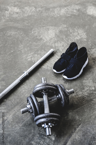 close-up shot of adjustable dumbbells with sneakers and empty bar on concrete surface