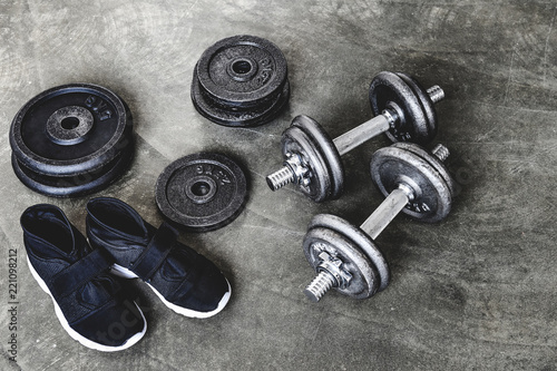 close-up shot of dumbbells with weight plates and sneakers on concrete surface