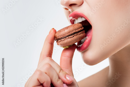 cropped view of woman biting chocolate french macaroon, isolated on white