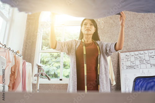 From below shot of lovely Asian woman laying piece of delicate fabric on table in tailoring workshop