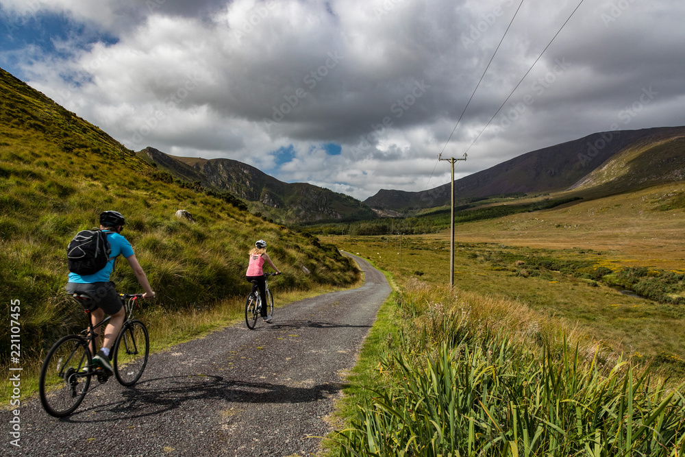 Fototapeta premium Active couple biking on a rural country road in the scenic mountain valley landscape of the Dingle peninsula, County Kerry in the Republic of Ireland