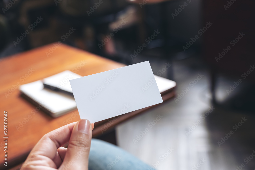 A hand holding white empty business card with notebook on wooden table A hand holding white empty business card with notebook on wooden table