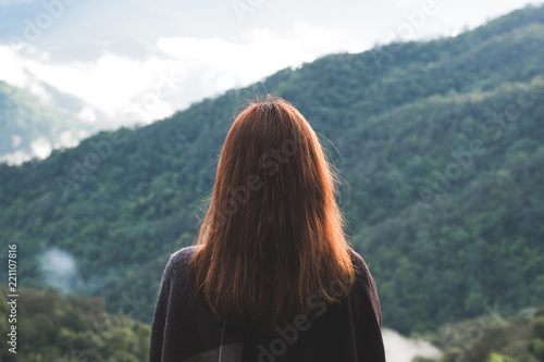 A woman standing alone and looking at mountains on foggy day with blue sky background in the morning