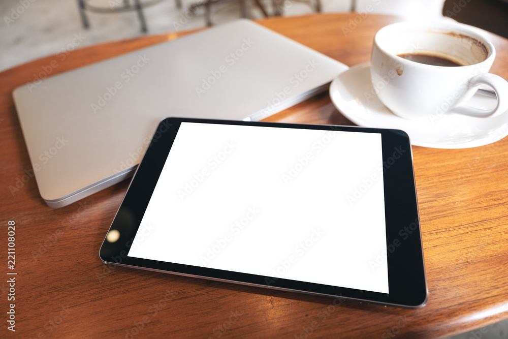 Top view mockup image of a black tablet pc with blank desktop white screen with laptop and coffee cup on wooden table Top view mockup image of a black tablet pc with blank desktop white screen with laptop and coffee cup on wooden table