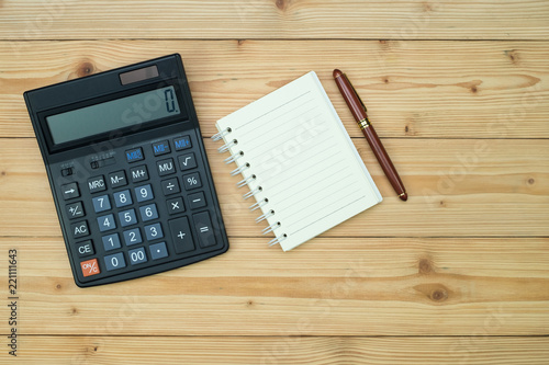 Office supplies or office work essential tools items on wooden desk in workplace, pen with notebook and calculator, top view