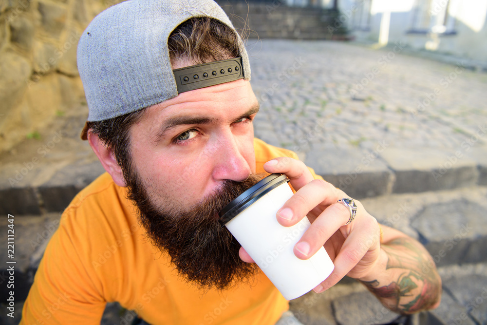 Man bearded hipster enjoy drink paper cup urban background. Hipster drink coffee to go while sit stairs outdoors. Urban food culture concept. Tasty sip concept. Tasty coffee tea in paper cup close up Man bearded hipster enjoy drink paper cup urban background. Hipster drink coffee to go while sit stairs outdoors. Urban food culture concept. Tasty sip concept. Tasty coffee tea in paper cup close up