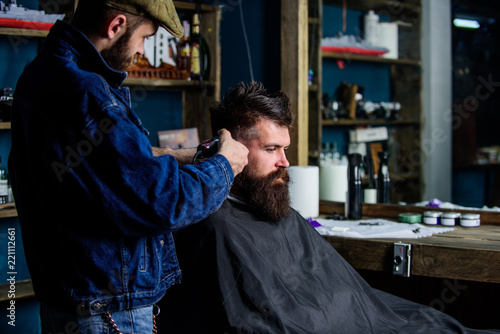 Hipster client getting haircut. Barber with hair clipper works on hairstyle for bearded guy barbershop background. Hipster lifestyle concept. Barber with clipper trimming hair on temple of client