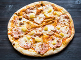 pizza with ham and pineapple on dark wooden board